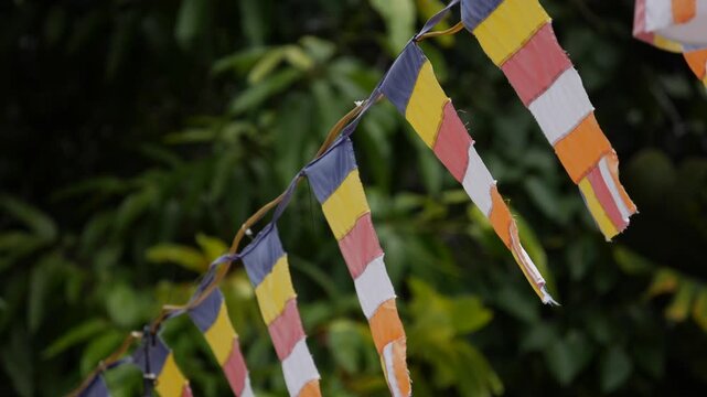 Colorful buddhist prayer flags wave in the wind against a soft green background. Religious symbolism.