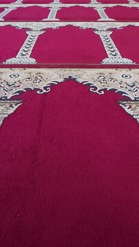 Patterned red prayer carpet arranged across mosque floor