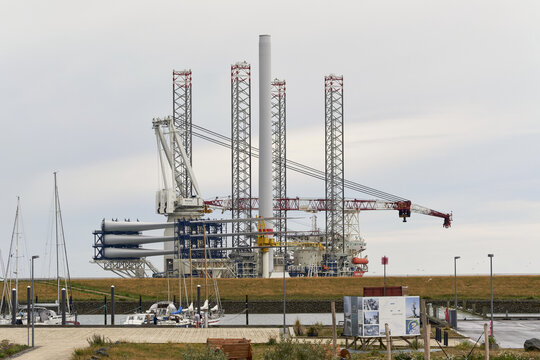 Esbjerg, Denmark - 31 July 2026: View of the Wind Keeper offshore vessel carrying wind turbine blades and a mast, seen from the marina dike with sailboats in the foreground.