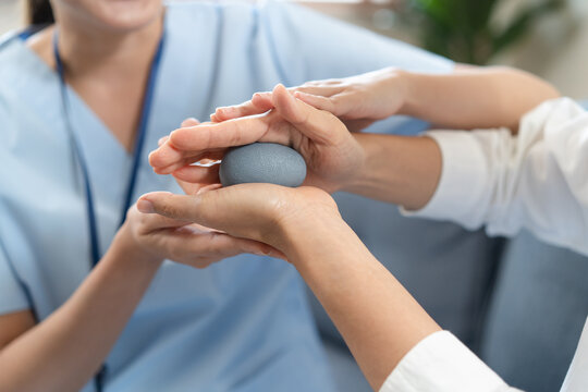 Professional physiotherapist assisting senior patient with hand rehab workout using squeeze stress ball at home medical care service concept