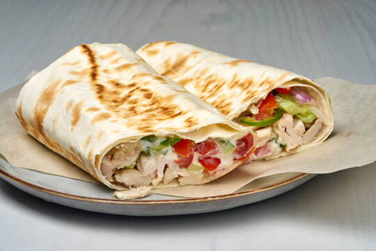 chicken wrap on a plate with parchment paper, fresh and appetizing top-down view, commercial food photography, healthy eating, white and brown colors, tortilla, chicken, vegetables.