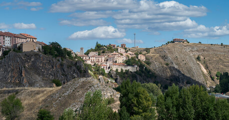Obraz premium A panoramic view of Sepúlveda, a historic hilltop village in Segovia, Spain, surrounded by dry hills, rocky cliffs, and a rural landscape under a blue sky with scattered clouds