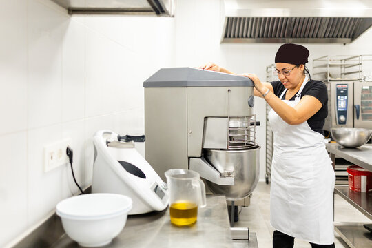 A pastry chef between 30 and 40 years old, wearing a hat and apron, is making cakes in a modern bakery.The woman is mixing the ingredients with an automatic mixer.Concept of Mexican cooks.