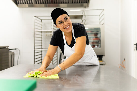 A pastry chef between 30 and 40 years old, wearing a hat and apron, is making cakes in a modern bakery.The woman is cleaning up after cooking with a cloth.Concept of Mexican cooks.
