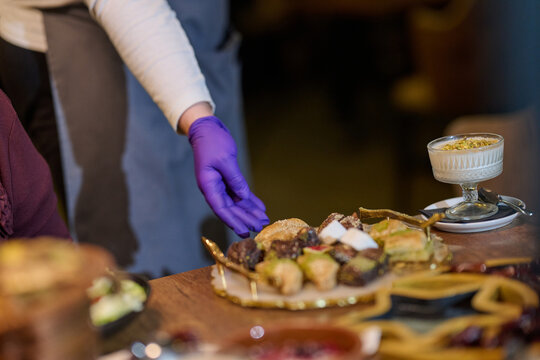 Gloved Server Serving Assorted Middle Eastern Desserts and Baklava On a Wooden Table
