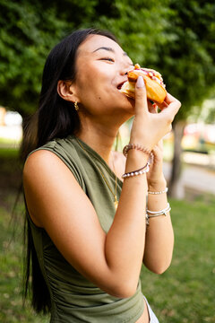 Vertical photo of a Korean woman between 20 and 30 years old eating a cake in an outdoor park. Concept of young girls eating outdoors.