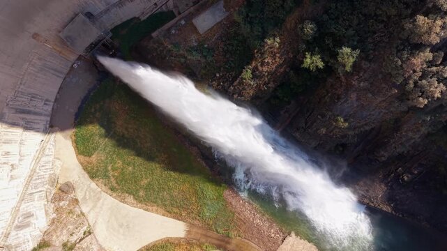 Top-down view of Baells Dam in Catalonia, Spain, showing a powerful water discharge cascading down the concrete structure into the rocky river valley below