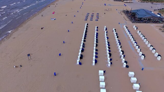 Aerial view video clip of Katwijk aan Zee beach resort, beach cabins, blue windbreak screens, Zee en Zon pavilion terrace, and North Sea waves in South Holland, Netherlands