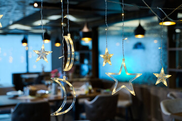 Obraz premium Hanging Star and Moon Christmas Lights Decoration in Cozy Restaurant Interior With Festive Bokeh