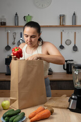 Woman in sportswear unpacking grocery delivery bags in her kitchen. Healthy eating, nutritious...