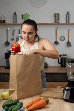 Woman in sportswear unpacking grocery delivery bags in her kitchen. Healthy eating, nutritious food, home shopping and wellness lifestyle