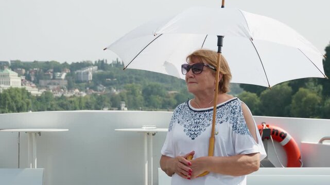 Senior female tourist holds a white parasol on a boat deck for solar protection. Aware of UV risks, she guards mature skin against photoaging, sunburn, and sun damage during summer travel.