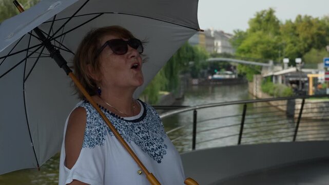 A senior female tourist admires historic landmarks overhead during a Prague river cruise. She enjoys gaining new impressions while exploring European sights from a unique perspective.
