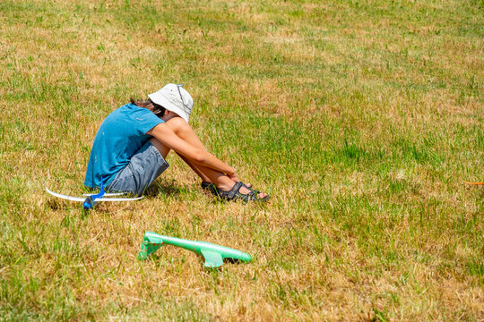 sad teenage boy sitting on dry grass in sunny park, foam glider plane, disappointment fun activity goes wrong, isolation outdoors, feeling exhausted, youth burnout, summer fatigue, adolescent stress