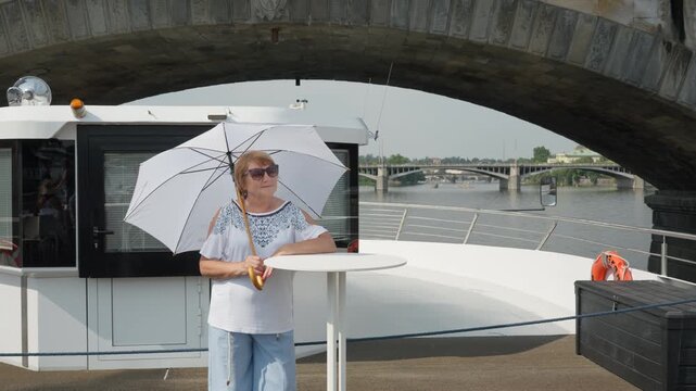 A tourist boat carries a senior woman under an arch of an old stone bridge in Prague. Sightseeing river cruise explores historic Czech architecture along Vltava. Summer European city tour.
