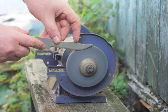 One male worker holds a knife in his hands and sharpens the iron blade on a grinding wheel on an electric sharpening machine on a table