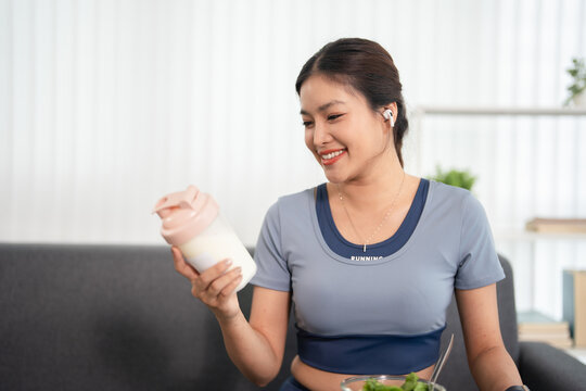 Young  woman in athletic wear with  whey protein shake after workout at home.