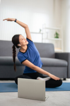 Young woman do excercise on a yoga mat at home, following a online workout tutorial on laptop.