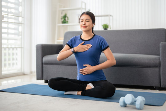 woman practices meditation with closed eyes and Hand on chest inliving room at home.