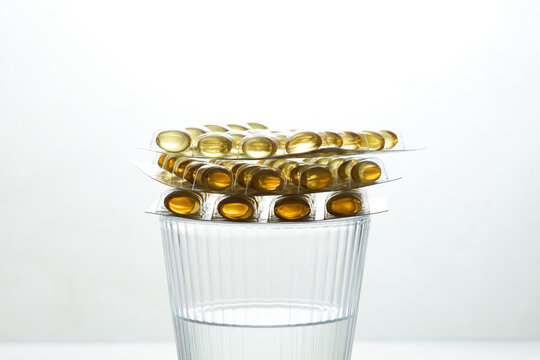 Blister Packs of Omega 3 Softgel Capsules Stacked on Glass of Water
