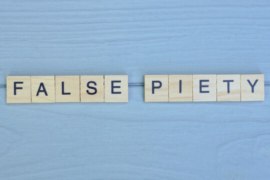 word false piety made from wooden gray letters lies on a gray background