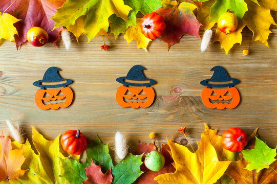 Halloween background - jack-o-lantern pumpkins with witch hats decorations surrounded by vibrant colorful autumn leaves on a wooden table, autumn background
