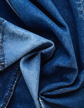Closeup of dark blue denim fabric with visible texture and stitching, abstract textile background with folds and highlights
