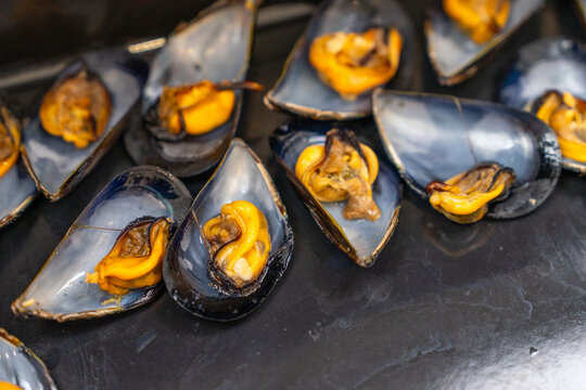 Rows of open blue shell mussels with plump orange flesh rest on a dark slate board, a fresh Mediterranean seafood starter rich in omega and healthy protein.