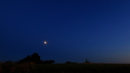 Moon on a twilight sky with stars, planets and landscape mountain silhouettes. © astrosystem