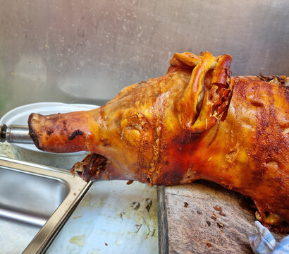 A close up of a traditional whole pig roasted on a spit with crispy golden brown skin on a wooden cutting board.