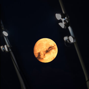 Golden full moon rising behind stadium lights at night, real atmospheric scene with deep blue sky and natural illumination.
