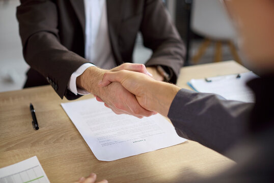 Handshake between businessmen partners and client advisor banker. They finalize agreement on a contract in an office with files and charts on the desk. Symbol of trust and successful partnership.
