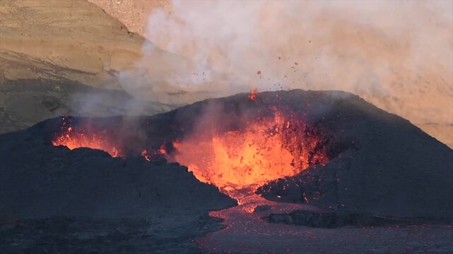 Aerial drone view of an active volcanic eruption in Iceland showing bright molten lava flowing from a volcanic vent across a dark basalt lava field with rising steam