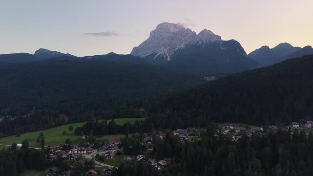 Drone view of Monte Antelao towering above the alpine forests and village of San Vito di Cadore during sunset in the Dolomites, Italy