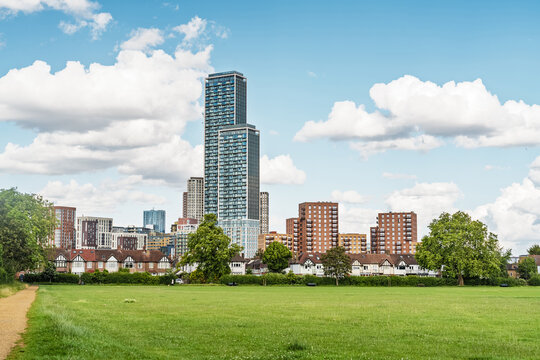 View of the modern skyline in Acton, featuring tall residential skyscrapers rising above traditional brick houses and a lush green park in London, England, United Kingdom.