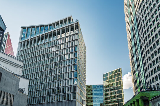 View of modern glass and steel office buildings with geometric facades under a clear blue sky in London, England, United Kingdom.