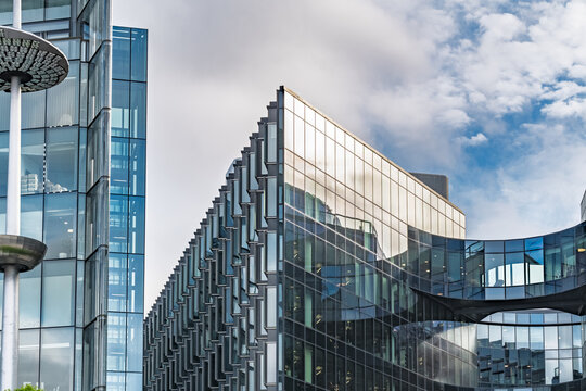 View of modern glass office buildings with reflective facades and a curved glass bridge structure under a blue sky in London, England, United Kingdom.
