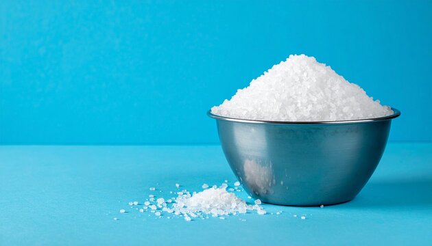 Metallic bowl of salt crystals, vivid blue background, purity