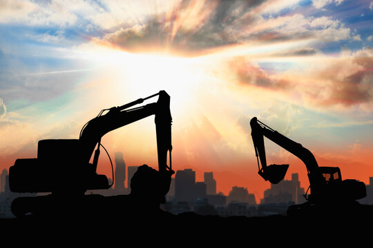 Two Crawler excavators silhouette are digging the soil in the construction site on   sunlight sky background .