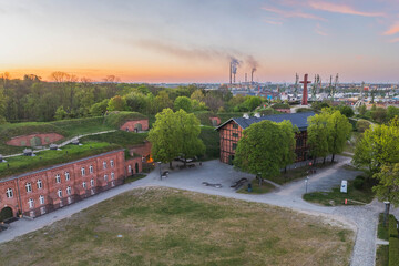 Aerial view of Góra Gradowa and Hevelianum in Gdańsk, Poland, with historic fortifications, greenery and the industrial harbor visible at sunset. © Kamil