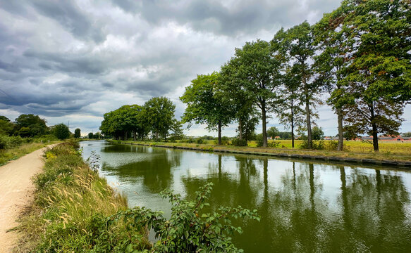 Rijkevorsel, Antwerpse Kempen, Belgium, overcast countryside canal with lined trees and walking path, cool tones and reflective surface, windswept vegetation and quiet