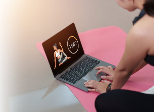 Woman on yoga mat using laptop for online fitness workout class at home