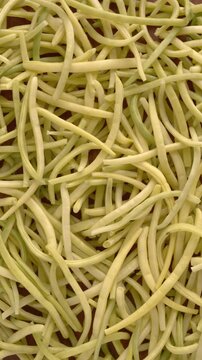 Background texture of freshly harvested yellow French beans (Golden Teepee variety) from your own garden, slow, smooth mechanical rotation, natural light; vertical video. 