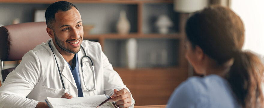 Smiling Male Doctor In White Coat Engaging With Female Patient During Consultation At A Healthcare Clinic. Both Displaying Positive Emotions, Fostering Trustful Doctor-patient Relationship.
