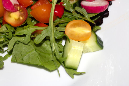 Close up of a delicious healthy side salad with leaves and radish on a white plate