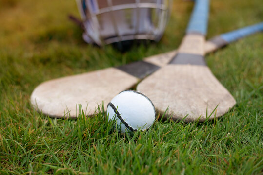 Worn wooden hurleys and sliotar rest on green grass beside a protective helmet, evoking Gaelic sport, Irish tradition and outdoor practice equipment for hurling players and teams.