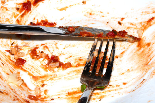 Close up of a messy dirty used white plate with cutlery on