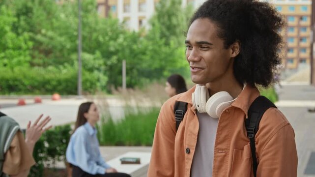 Black young adult male student greeting Caucasian classmate with handshake and hug on university campus. Ideal for higher education marketing, student life videos, and diversity campaigns