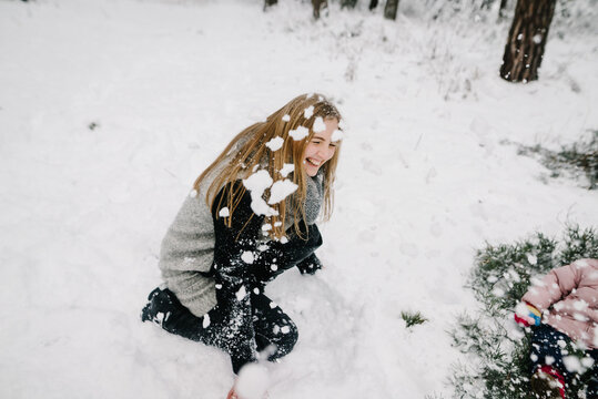 Happy mother playfully throwing snow in winter forest, making her little child laugh. Joyful family emotions and winter walk.