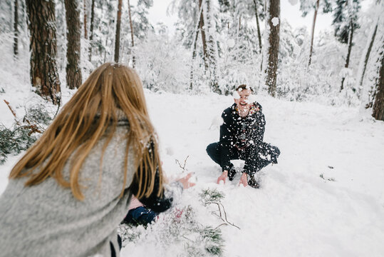Young couple playing snowballs in winter forest, enjoying active leisure outdoors. Happy emotions and family idyll in snowy atmosphere. Closeup.